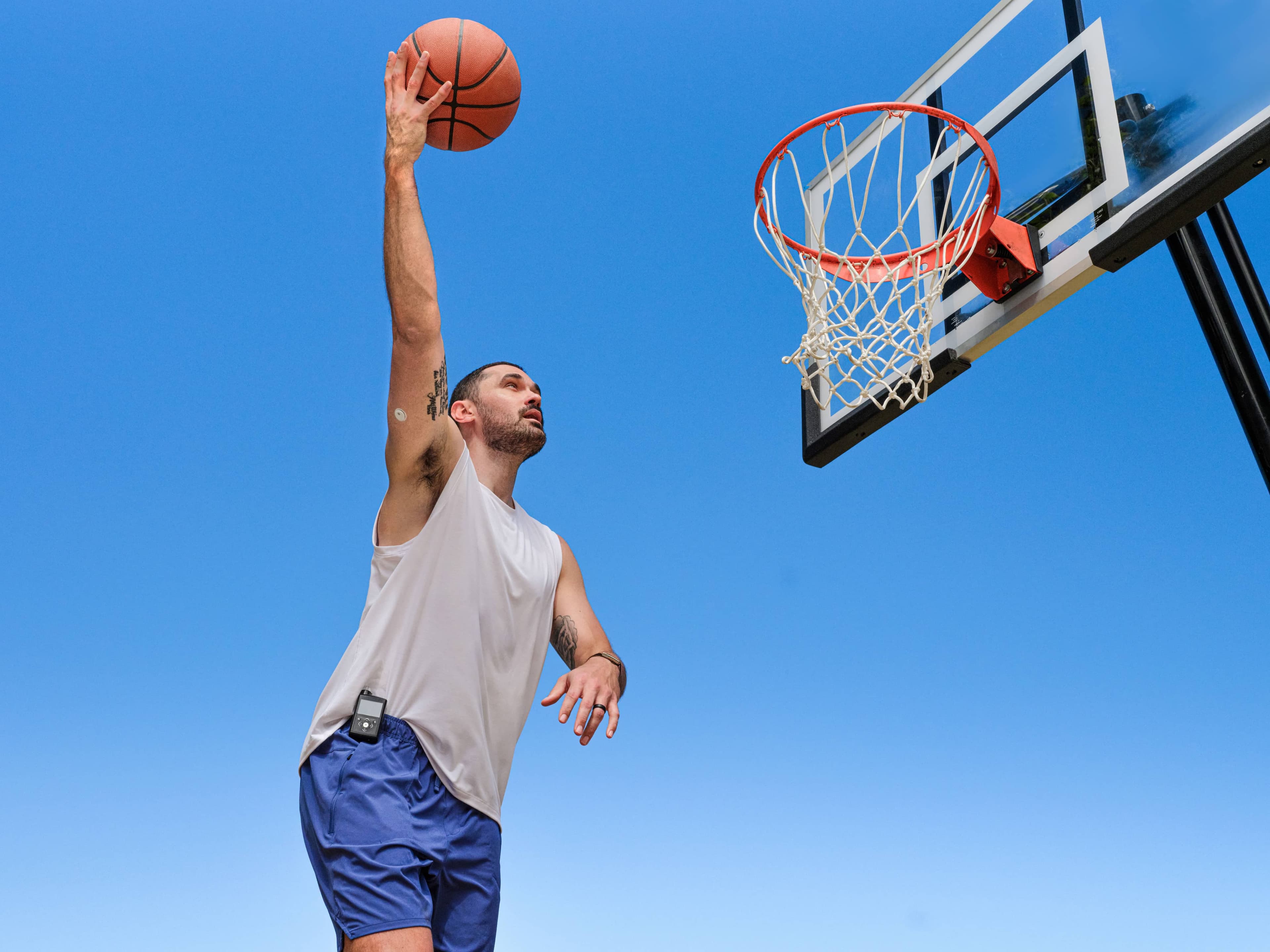 Man dunking a basketball on an outdoor court wearing the MiniMed™ 780G insulin pump and Instinct™ sensor on his upper arm