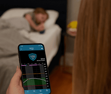 Adult holding a smartphone displaying the MiniMed™ CareLink app while a child sleeps in the background