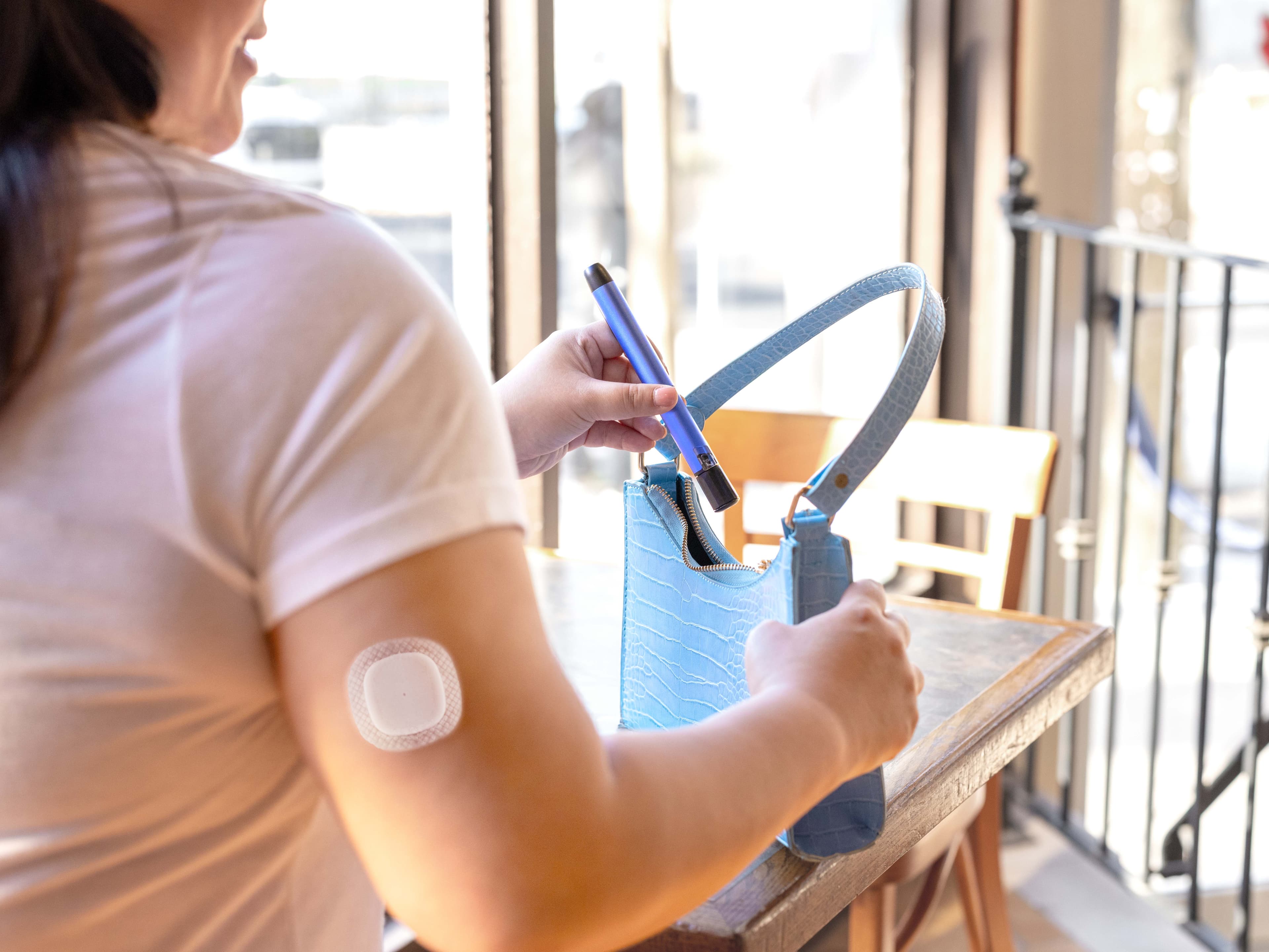 Person with CGM sensor on arm placing MiniMed™ InPen smart insulin pen into a handbag in an everyday setting