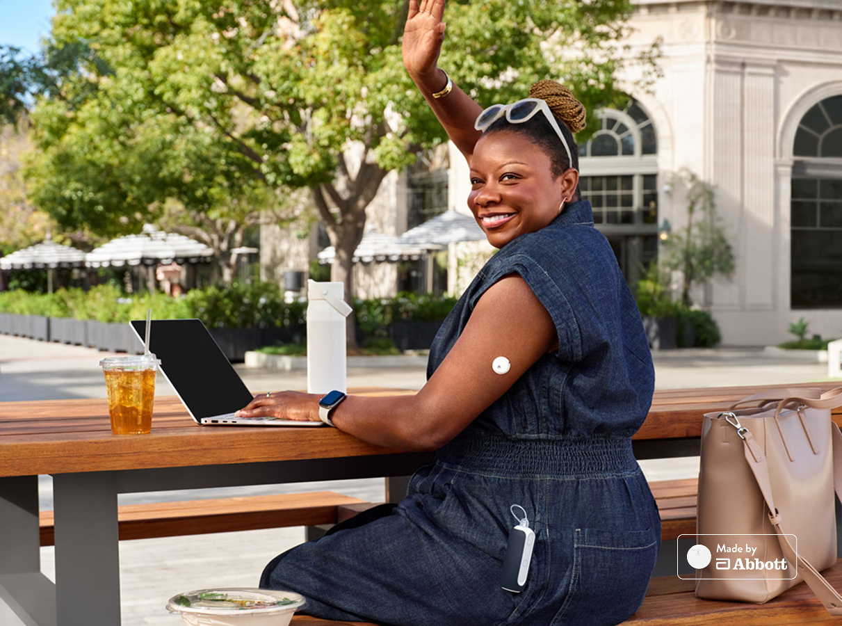 Woman sitting at picnic table wearing Instinct sensor and working on laptop