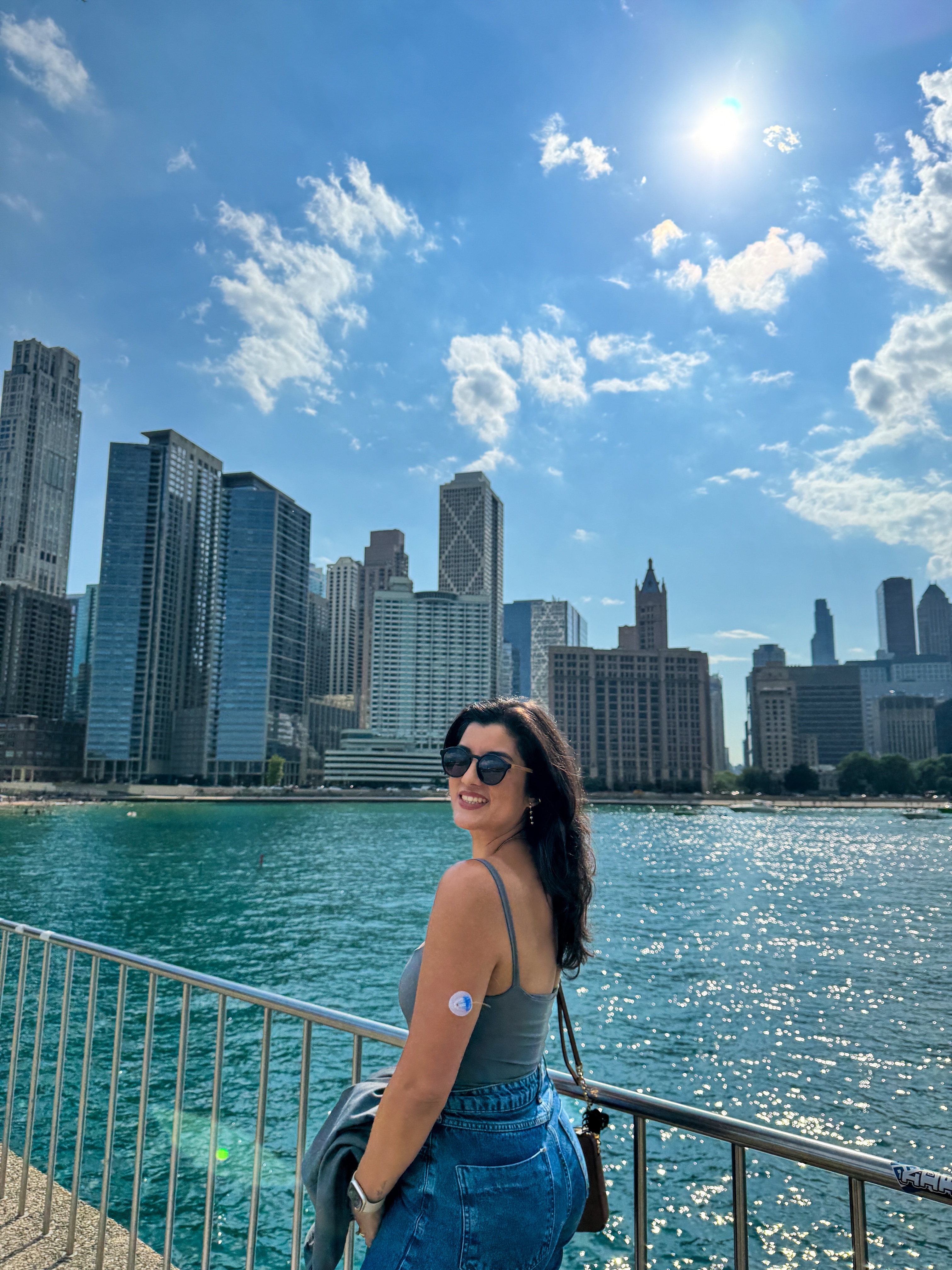 Daniela standing by a waterfront with a city skyline in the background on a sunny day.
