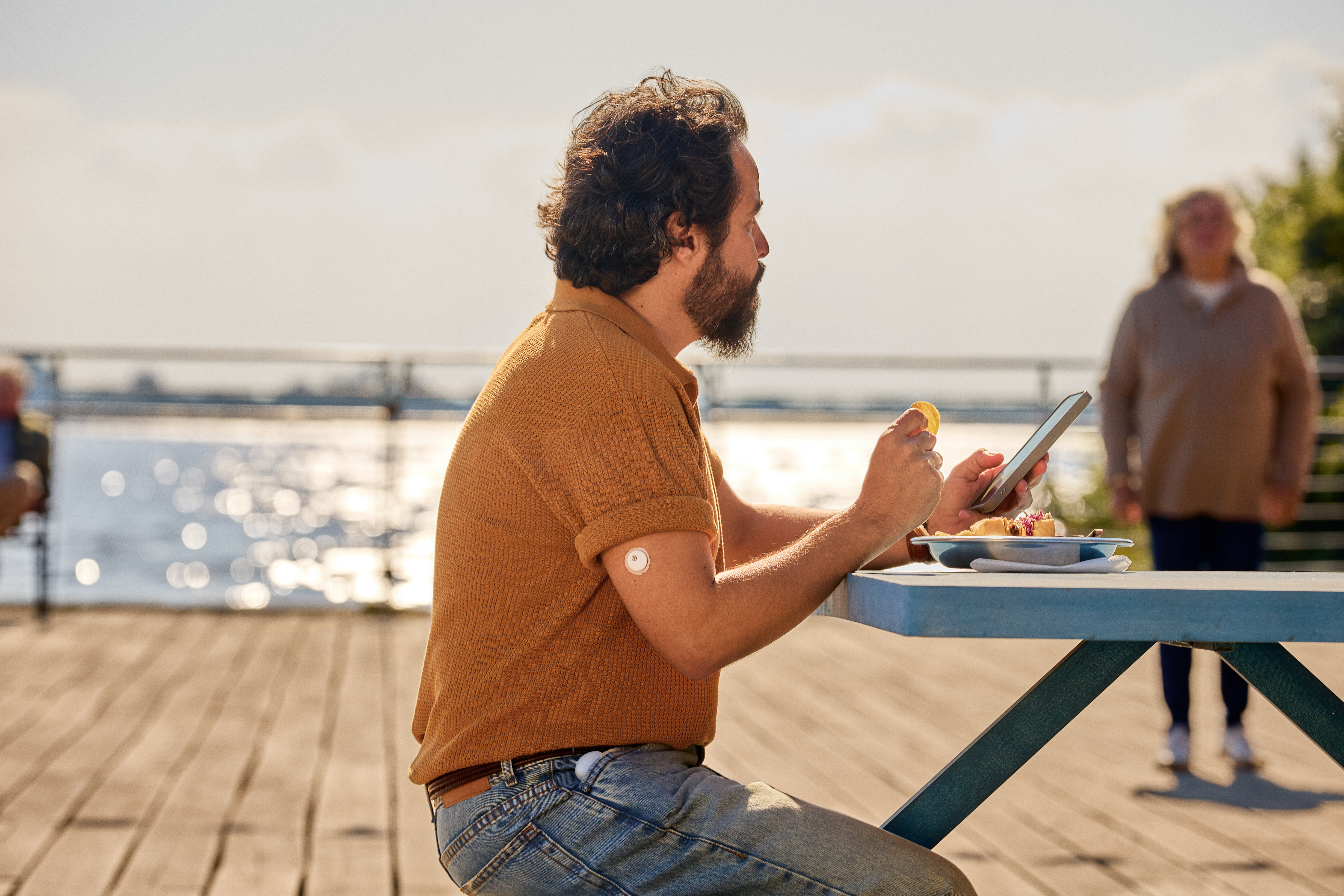 Man eating at pier holding phone wearing Flex and Instinct sensor, 